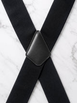 Black suspenders with a textured fabric strap and a stitched black leather-like central connector, laid out on a white marble surface.