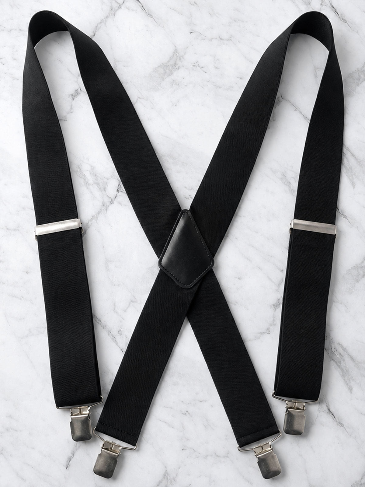 Black heavy duty work suspenders suspenders with silver metal clips, laid flat on a white marble background.