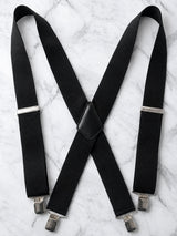 Black heavy duty work suspenders suspenders with silver metal clips, laid flat on a white marble background.