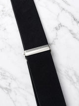 A close-up of a black woven elastic strap with a polished silver metal slider clasp, laid diagonally on a white marble background.